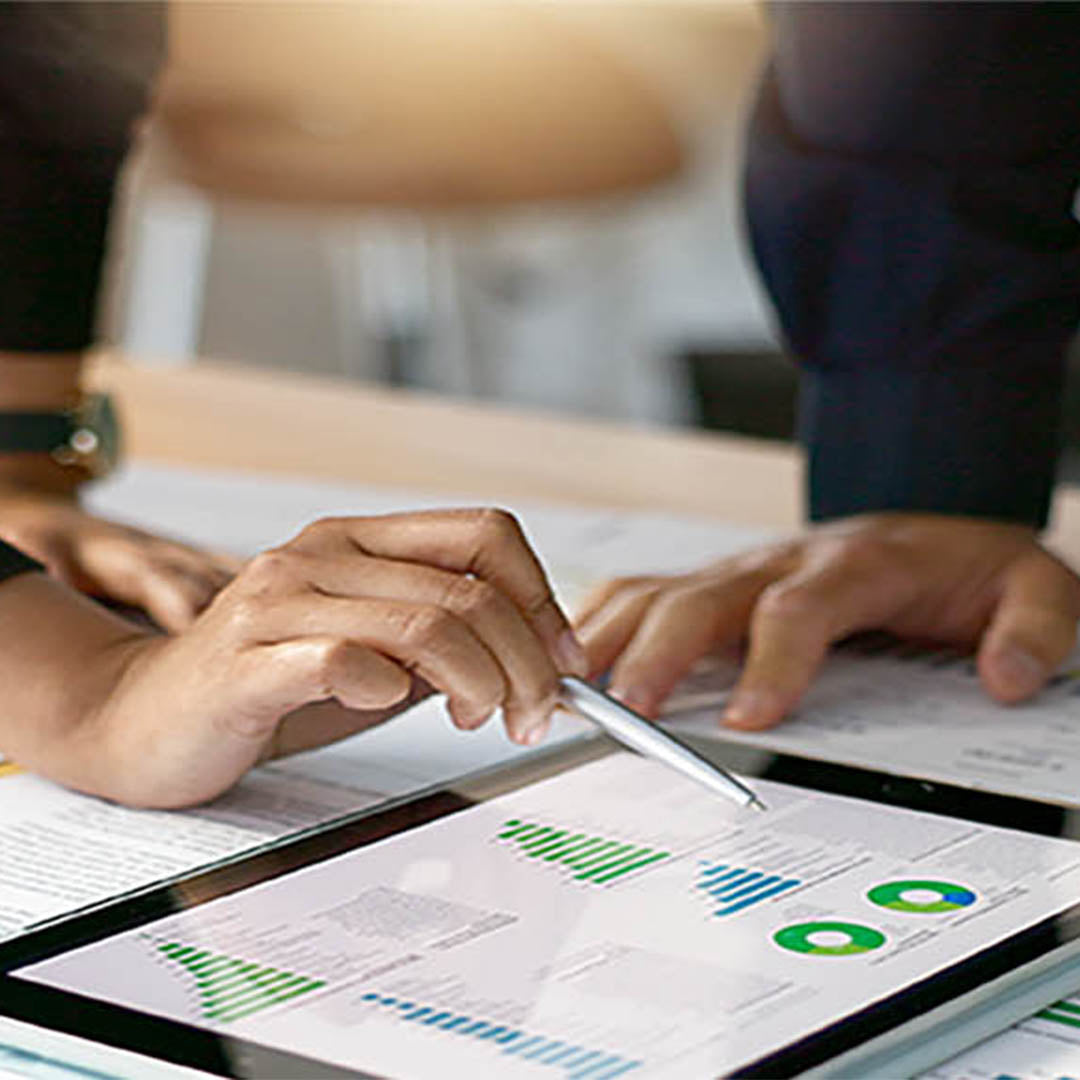 Two people working on financial documents with a tablet displaying graphs.